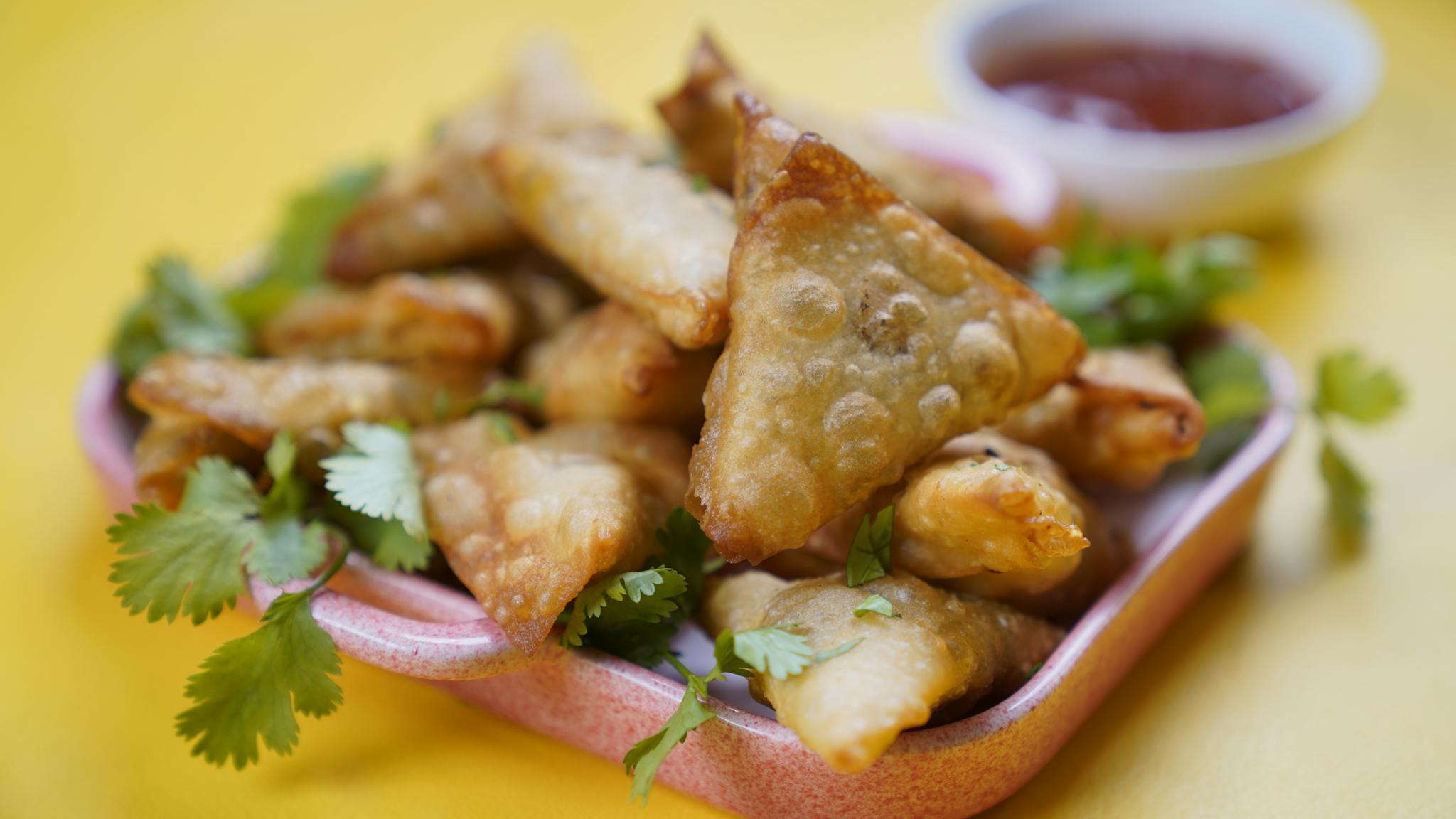 A plate of golden, crispy samosas garnished with cilantro, served with a side of dipping sauce.