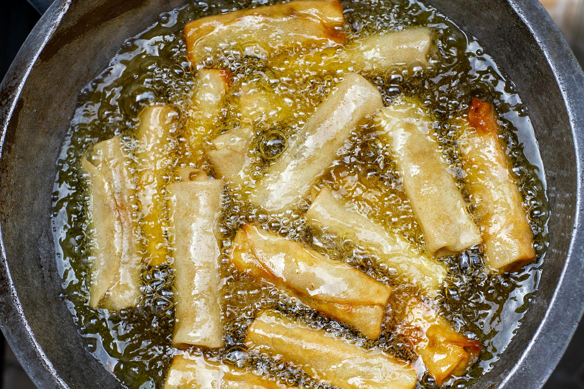 Close-up of golden spring rolls frying in hot oil, showcasing delicious texture and crispy edges.