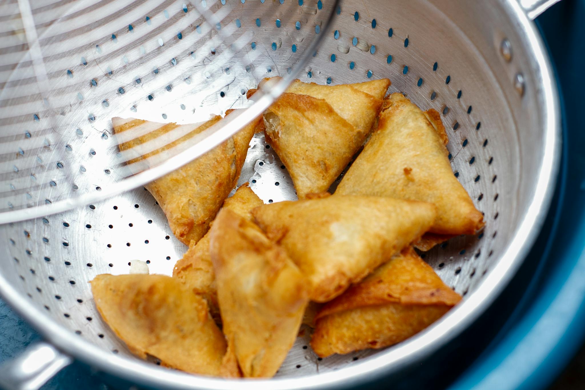 Delicious golden samosas in a metal colander, perfect for snack lovers.