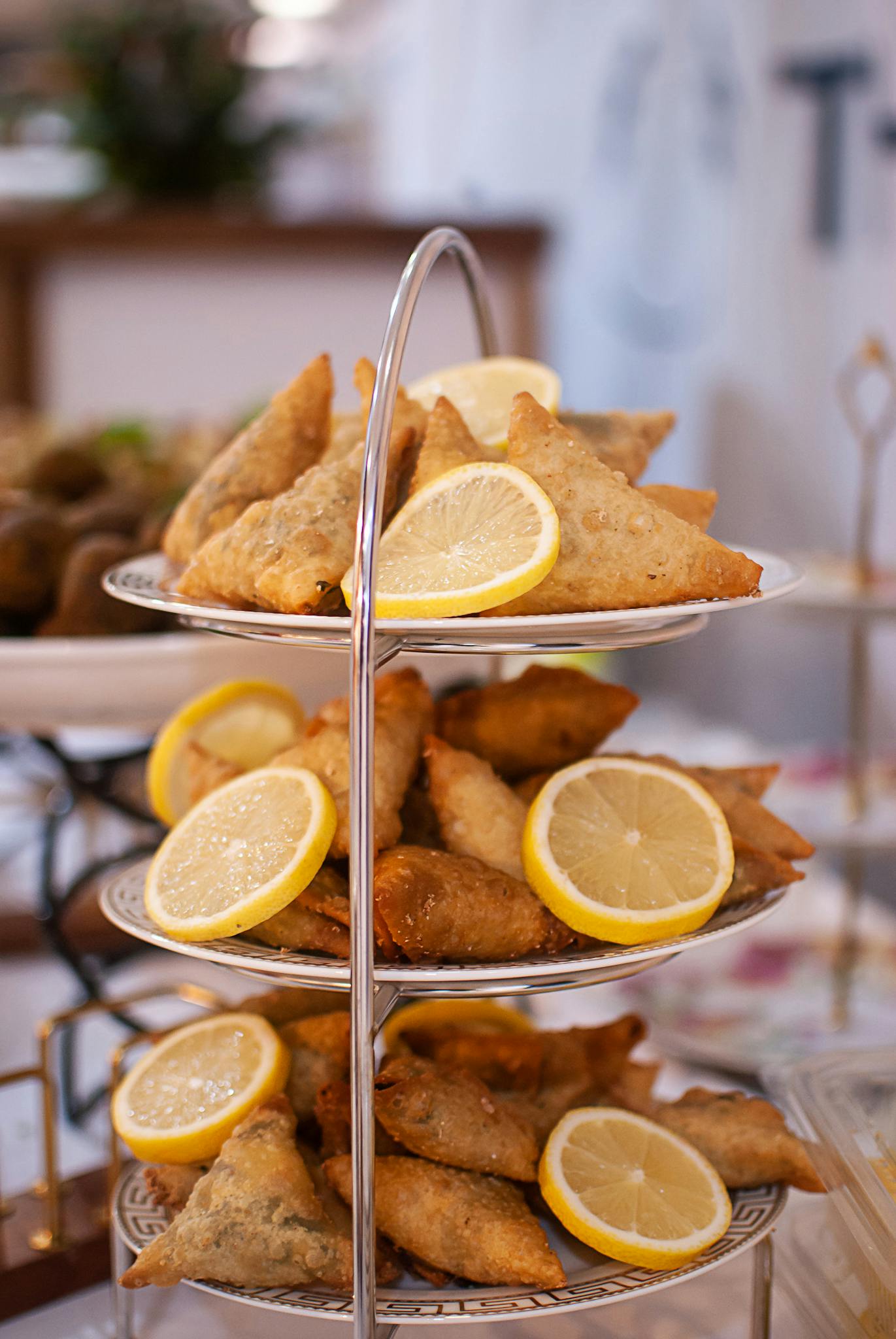 Three-tiered tray showcasing appetizing fried samosas garnished with lemon slices in a bright, inviting setting.
